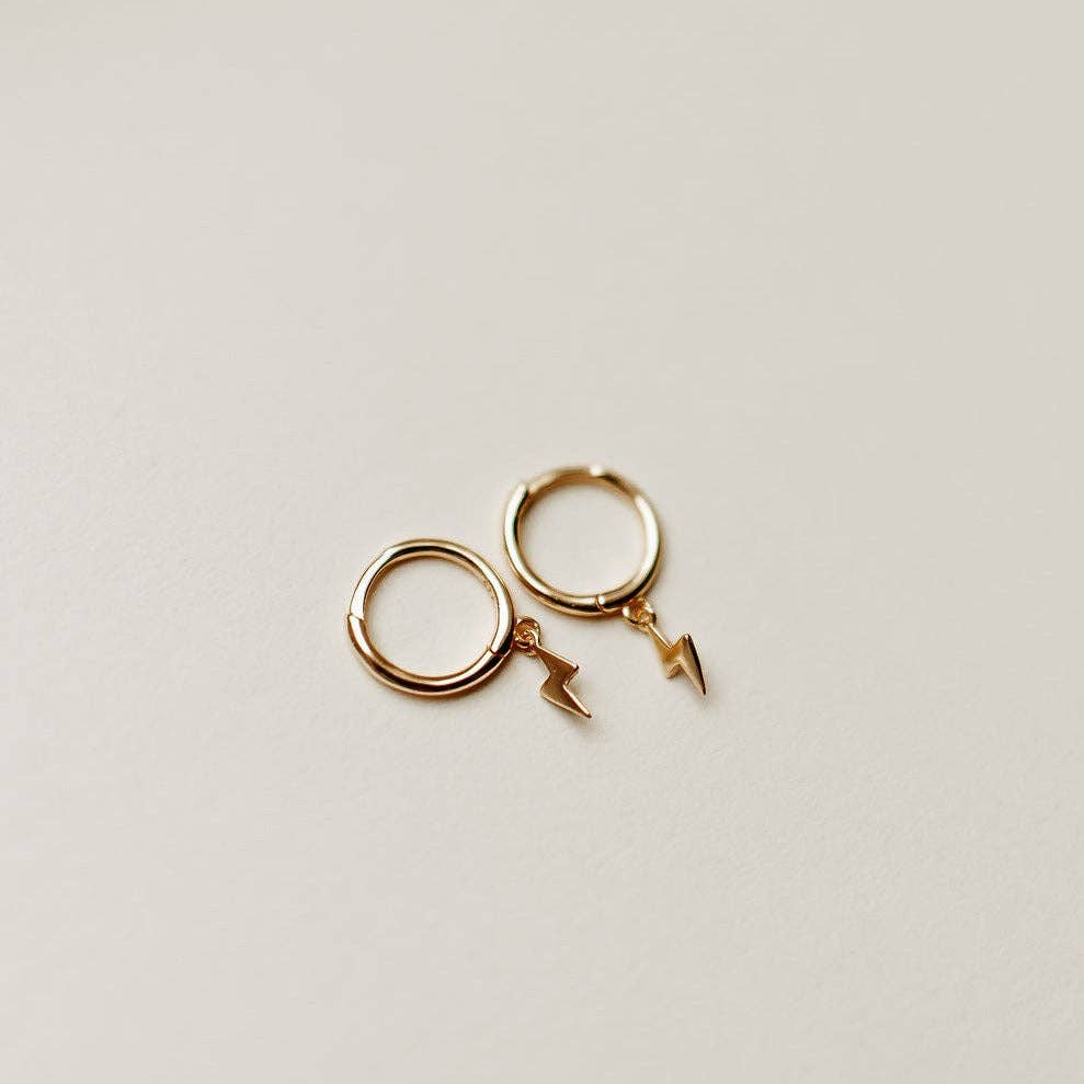 Gold hoop earrings with lightning bolt charms on a light beige background
